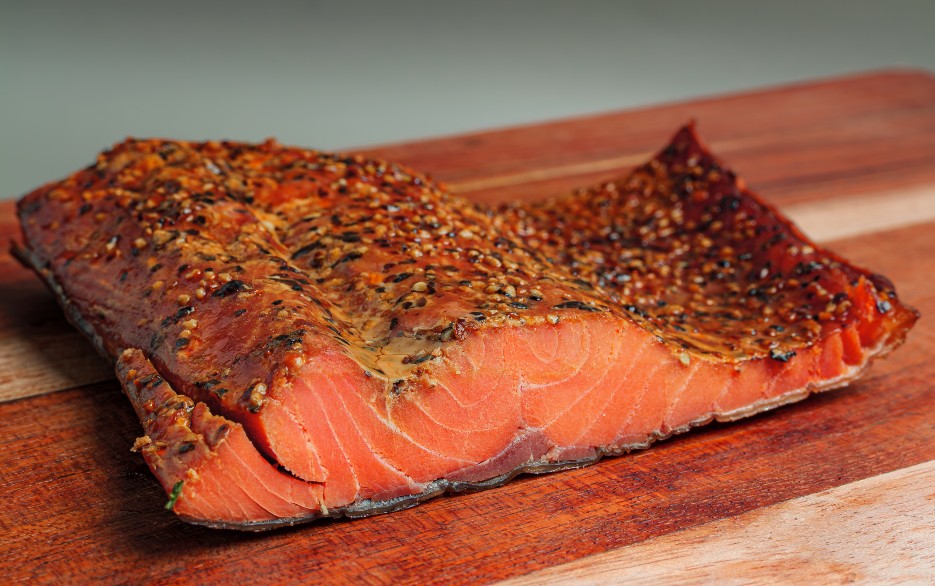 Wild Smoked Coho Salmon - Black Pepper variety, vacuum-sealed by Long House Fish Co. with red label on rustic wood