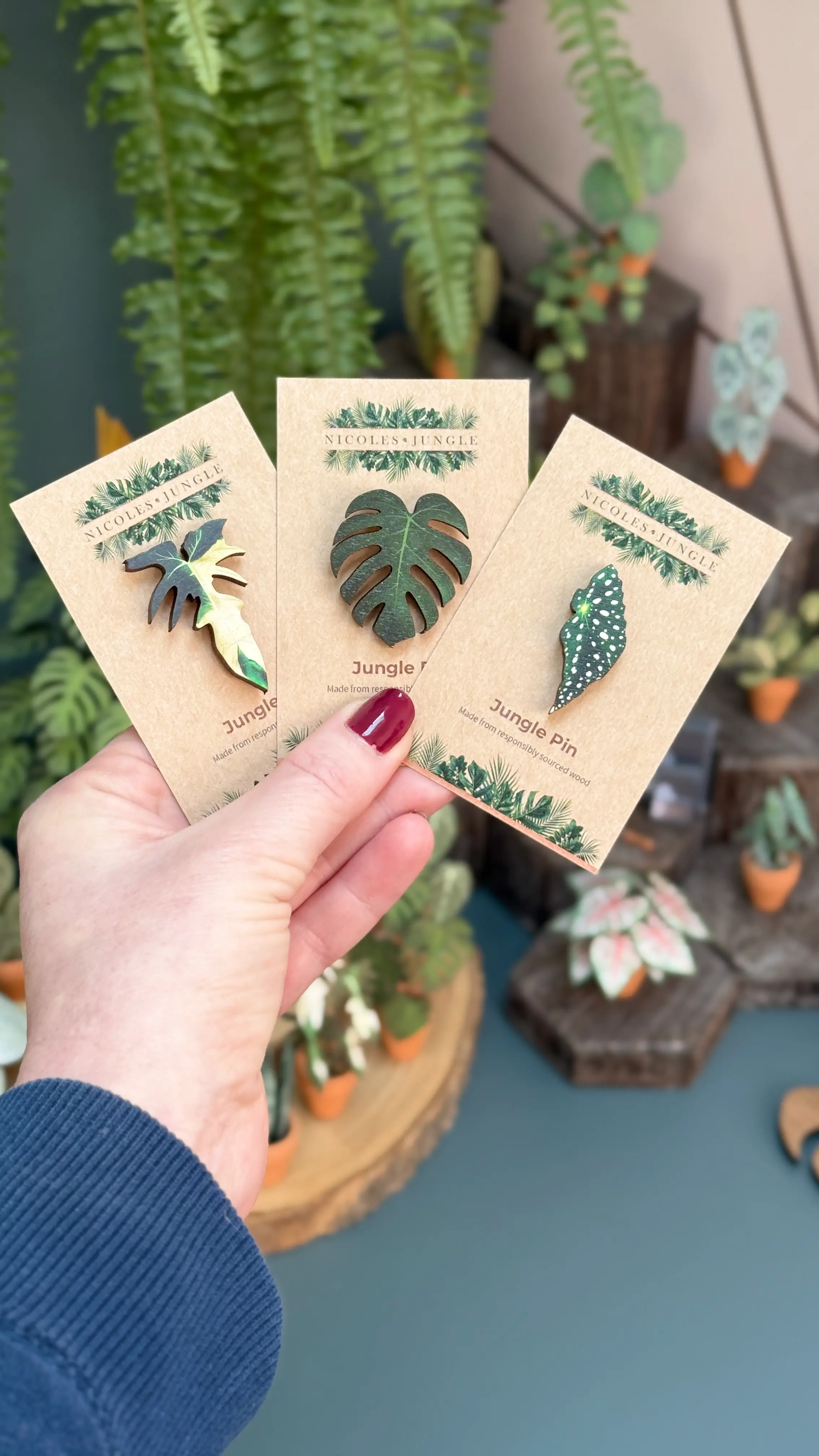 Hand holding three Nicole's Jungle wooden plant pins on branded backing cards.