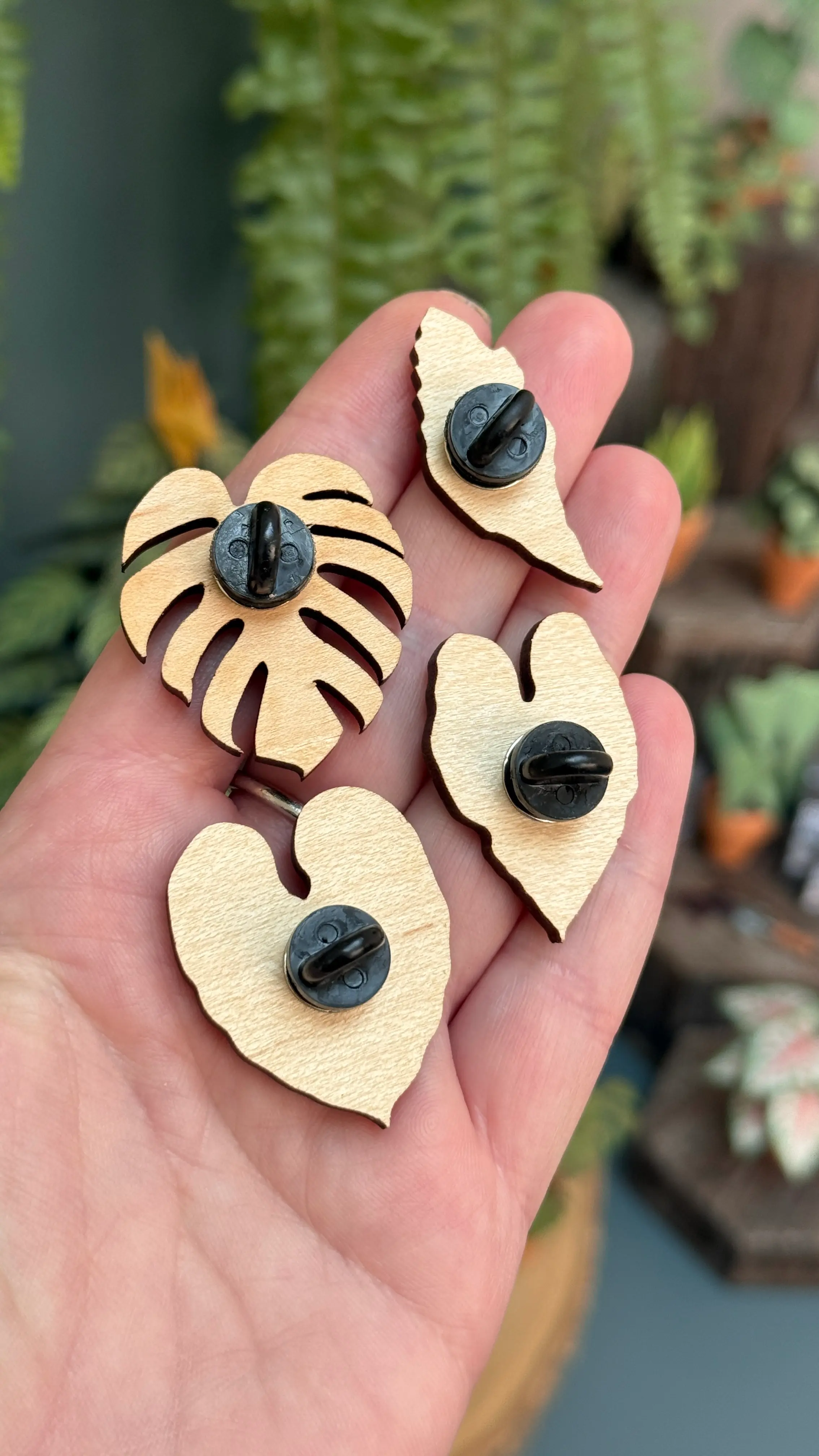 Back of four Nicole's Jungle wooden plant pins resting on a hand, showing black pin fastenings.