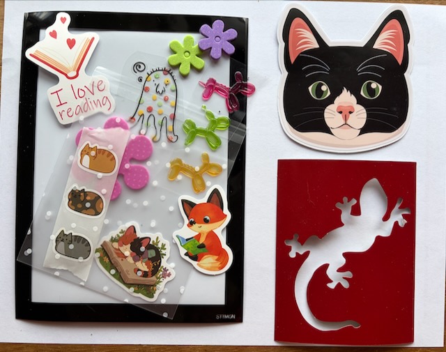 A flat-lay of kid-friendly happy mail goodies: cat and gecko stickers, a fox bookmark, and 'I love reading' stickers