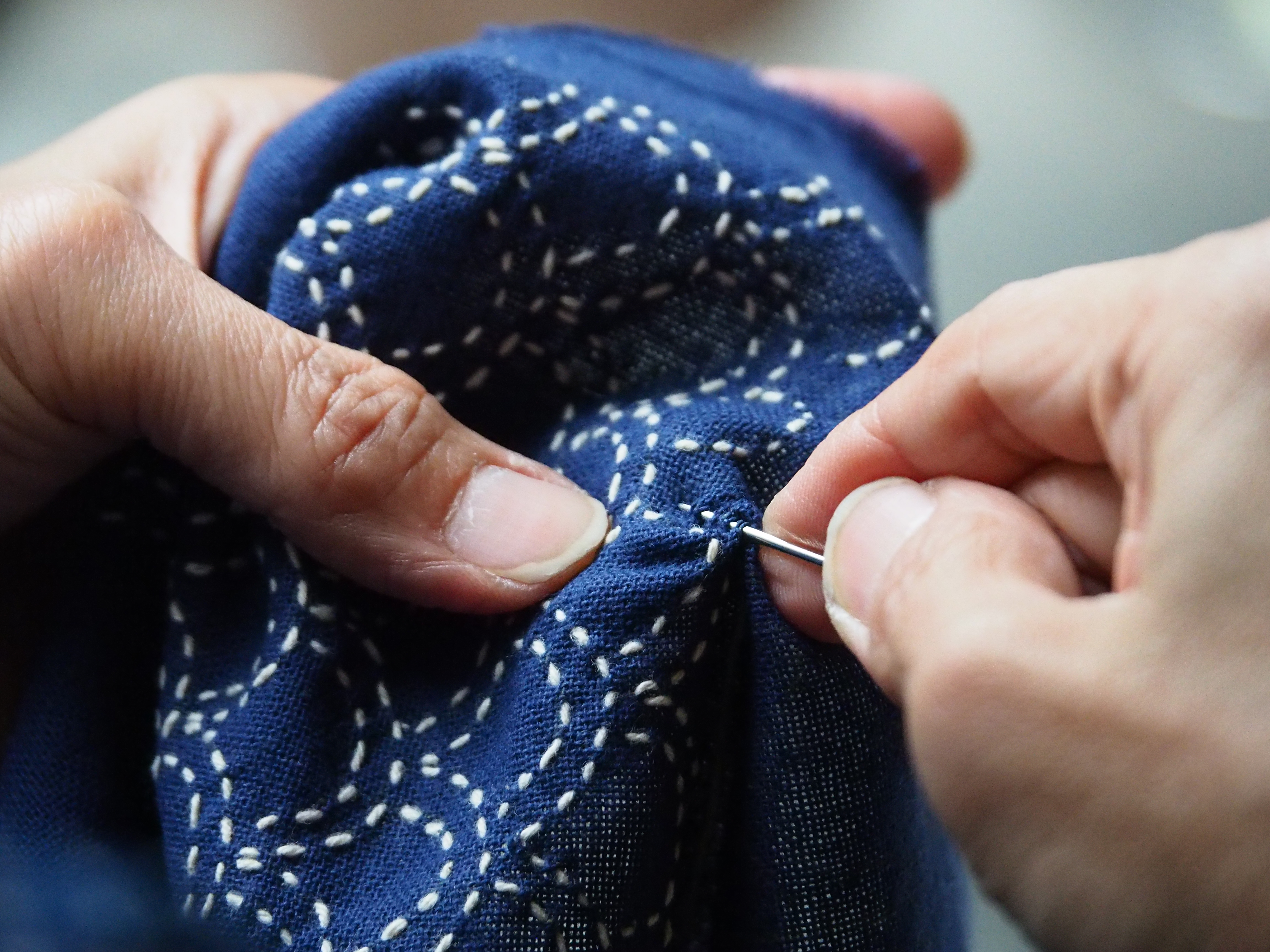 A close-up of indigo sashiko stitching on natural fabric