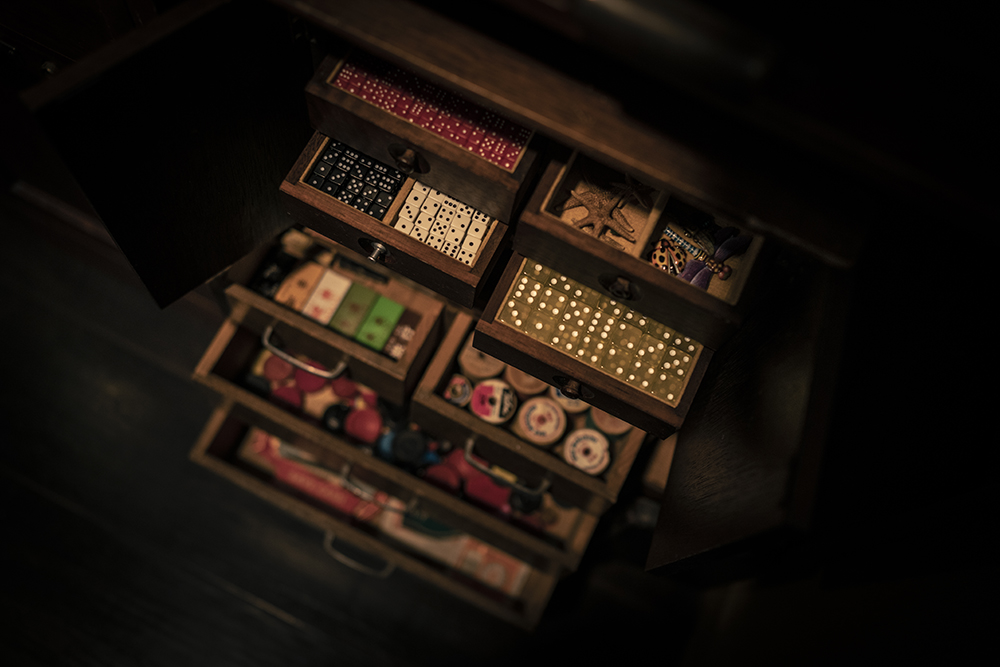 Open drawers filled with dominoes, spools, and tiny curiosities from the collection