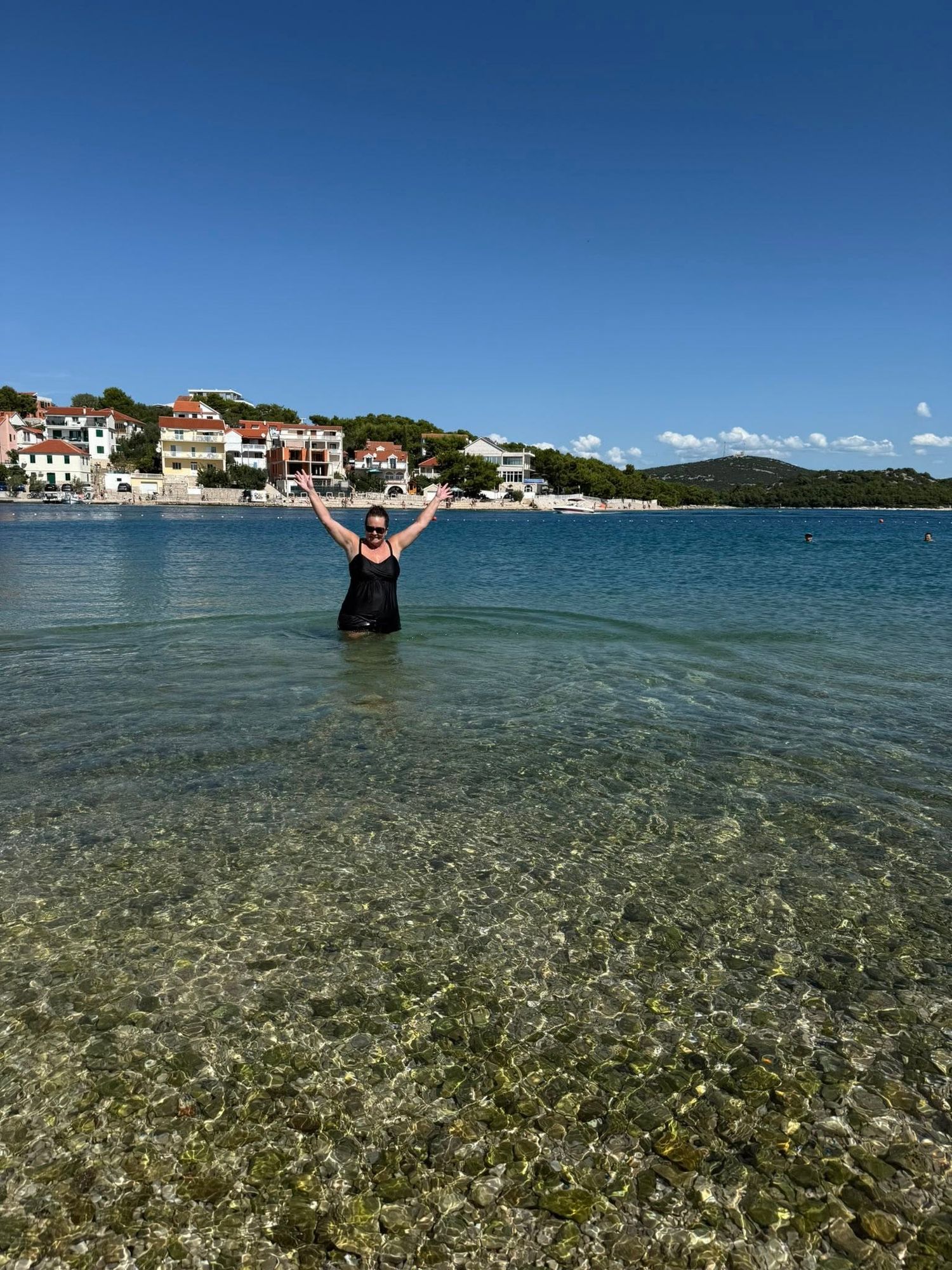 Traveler swimming in clear coastal water with a seaside village and mountains in the background